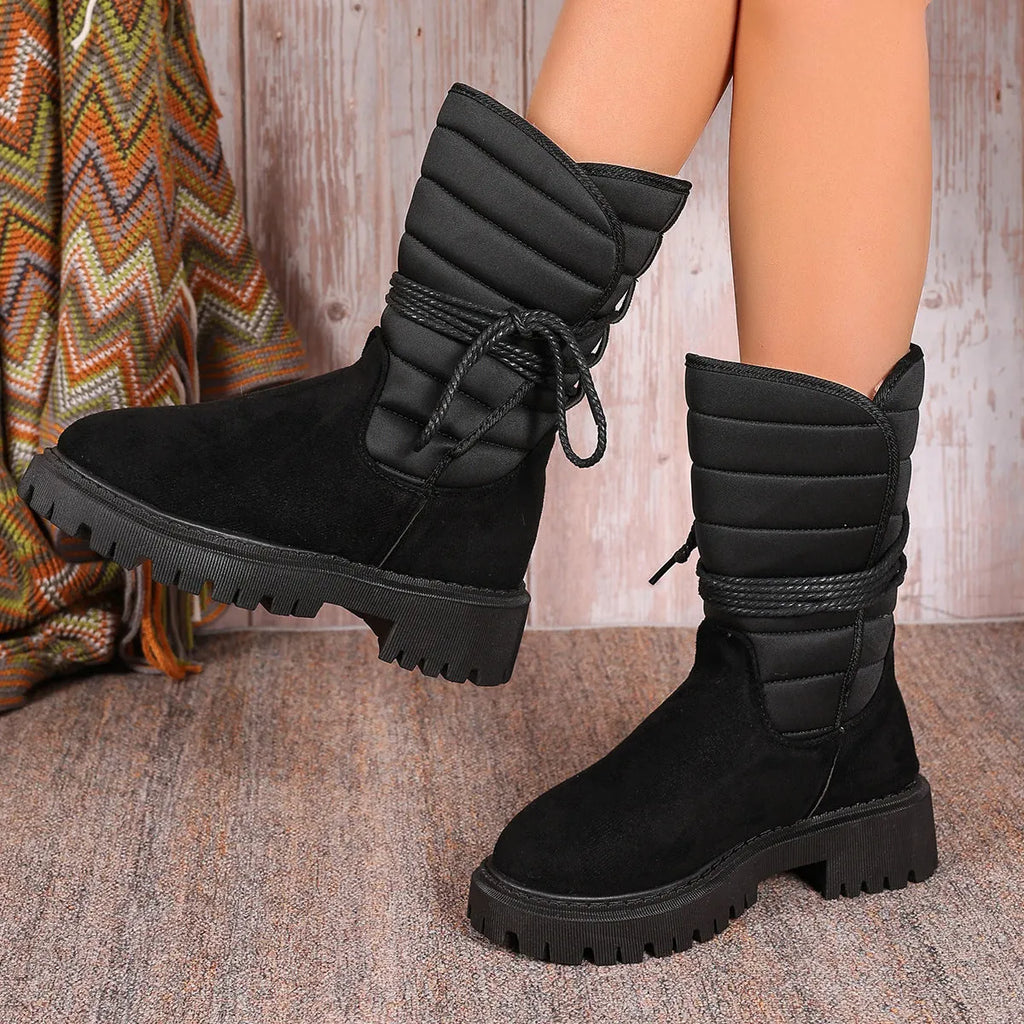 Women's black suede chunky heel snow boots with lace-up front and fleece lining shown on a winter background.