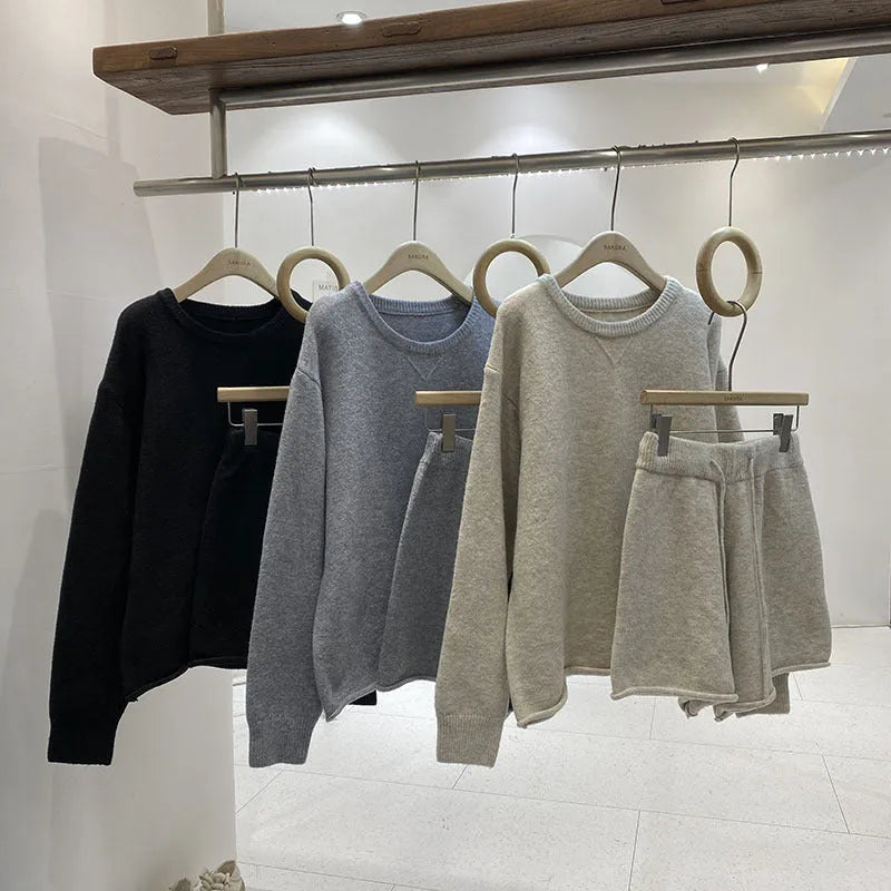 Woman wearing a loose grey long sleeve sweater and matching wide leg knit shorts lounge set.