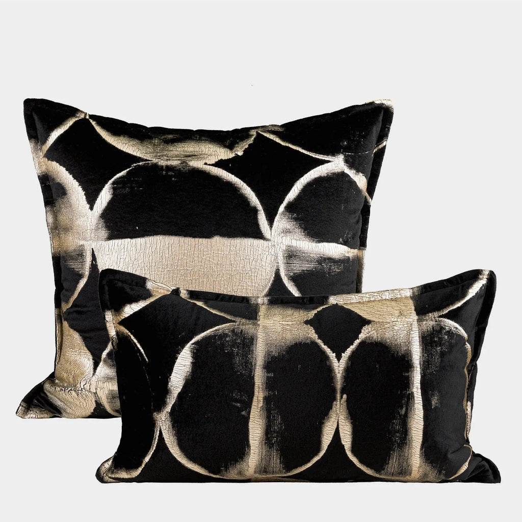 Black and gold abstract patterned square decorative pillow with a flannel cover on a grey sofa.