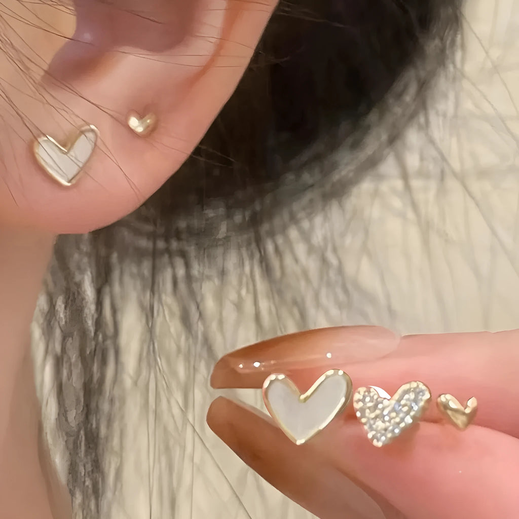 Three pairs of heart-shaped alloy earrings with electroplated finishes in gold, black, white, or pink colours.