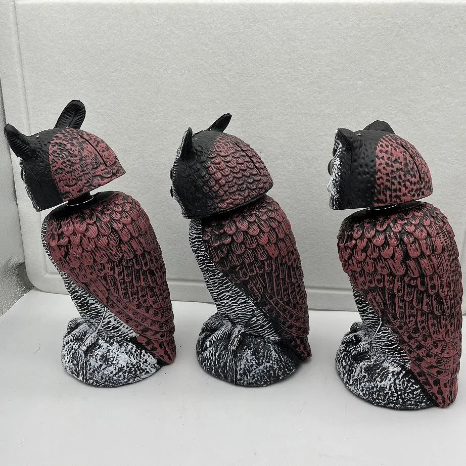 Artificial owl bird scare decoy ornament with a shaking head, shown in a garden setting.