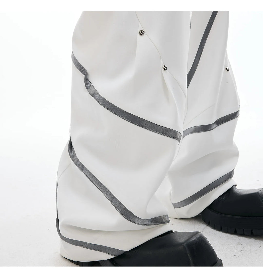 Men's black polyester trousers with metal striped rivets and pleated detail on a white background.