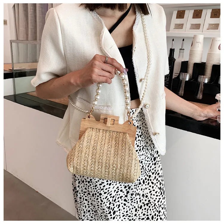 Women's woven straw shoulder bag with pearl chain detail in beige, showing horizontal square shape and single strap.