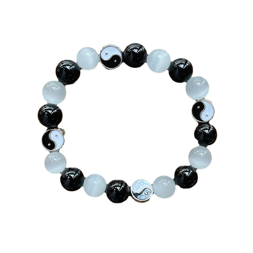 Close-up of a polished opal Tai Chi beaded bracelet with black agate ornamentation on a wrist.