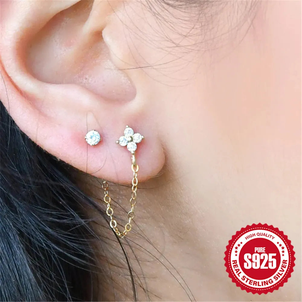 Close-up of a sterling silver stud earring with a geometric flower shape and dangling gold-tone tassel and chain details.