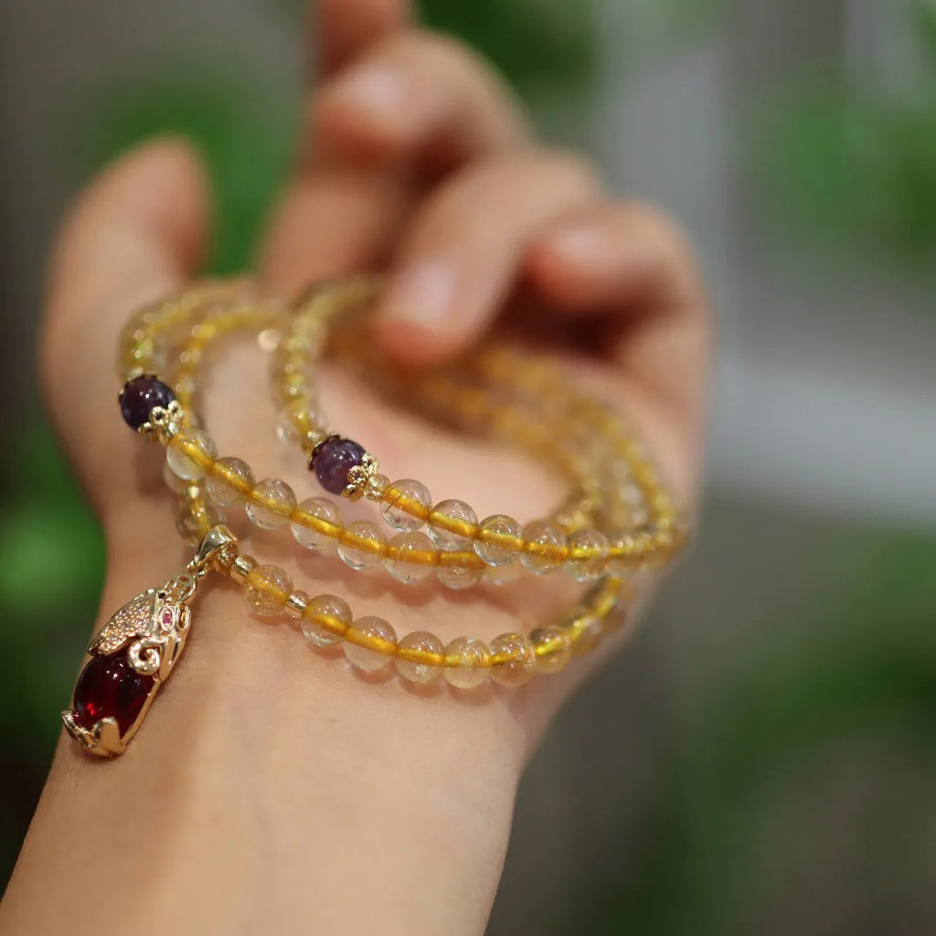 Handmade bracelet with Brazilian rutilated quartz beads, three gold circles, and a hanging bead pendant.