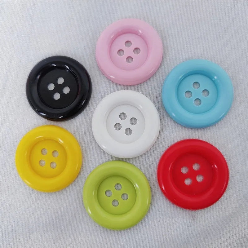 Assortment of oversized round plastic buttons with four holes in various colours and sizes on a white background.