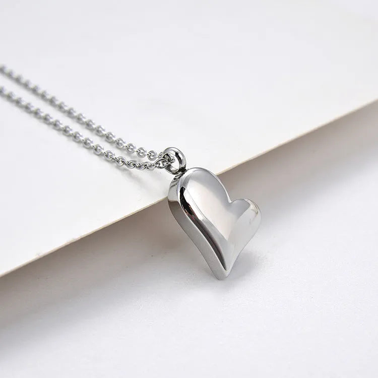 Silver-colour stainless steel necklace with a curved peach heart pendant on an adjustable chain.
