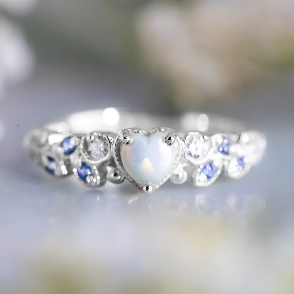 Women's white alloy heart ring with floral opal ocean detailing, shown on a finger.