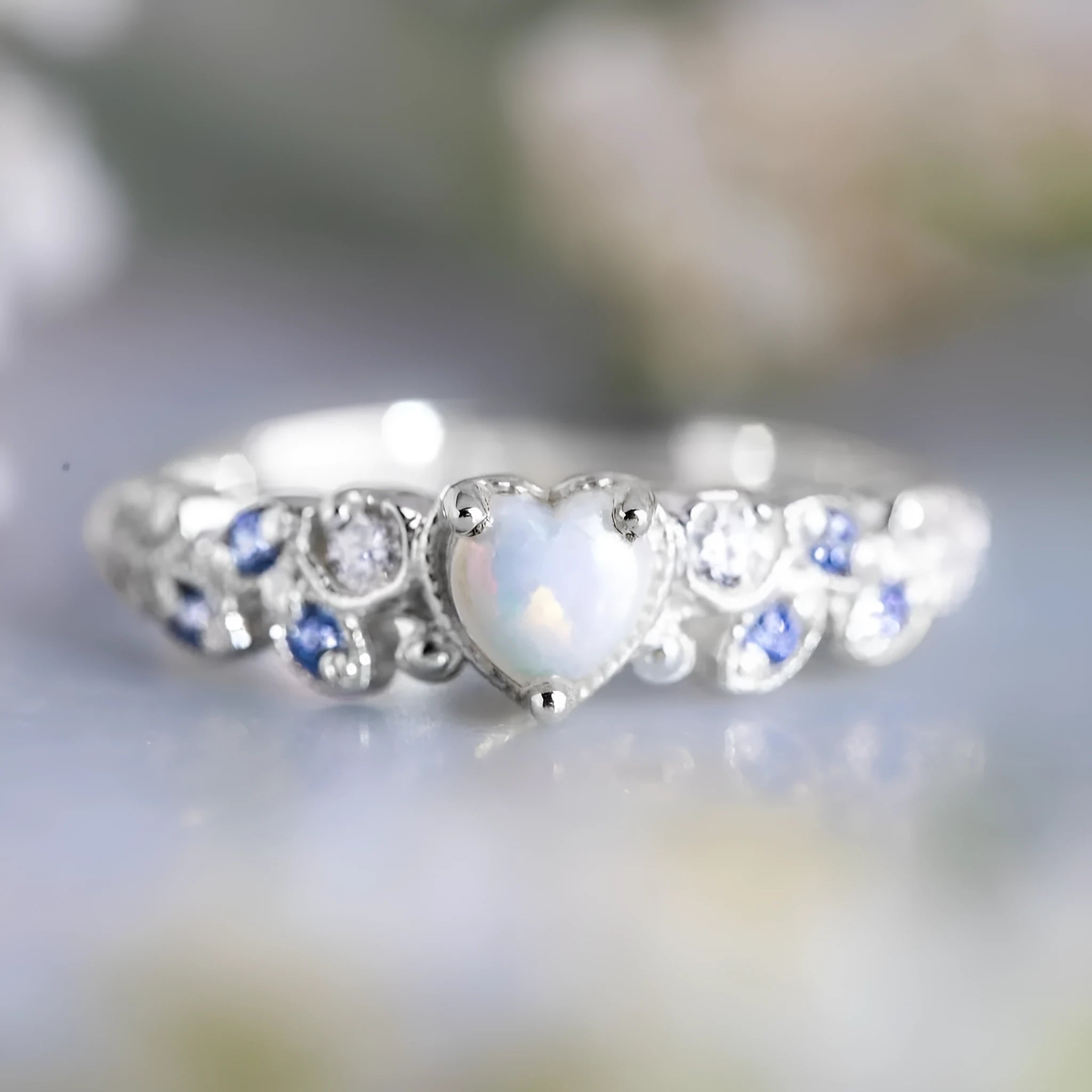 Women's white alloy heart ring with floral opal ocean detailing, shown on a finger.
