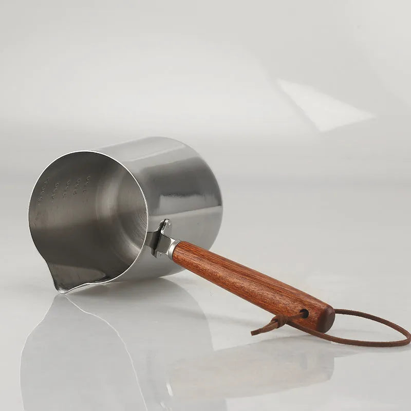 Stainless steel milk jug with measurement scale and wooden handle for barista latte art.