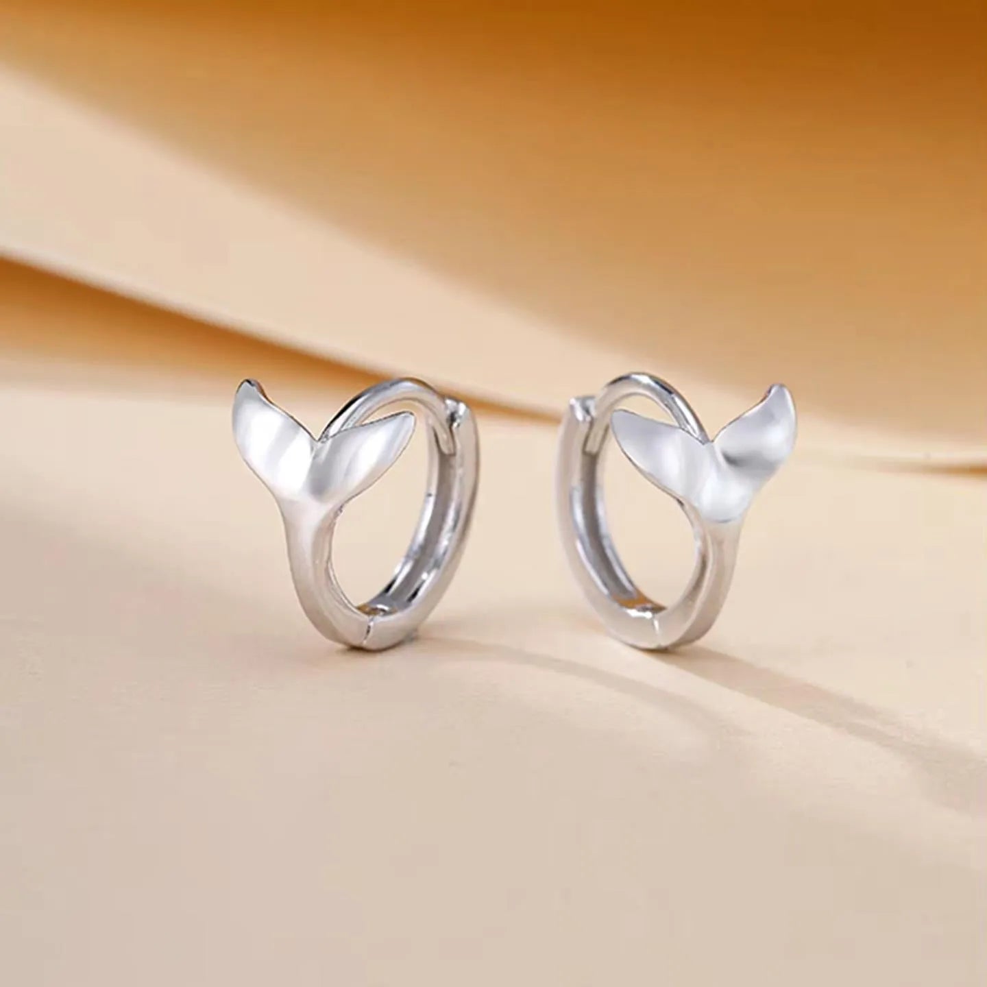 A pair of women's fishtail design earrings in copper with a white gold or yellow gold electroplated finish.