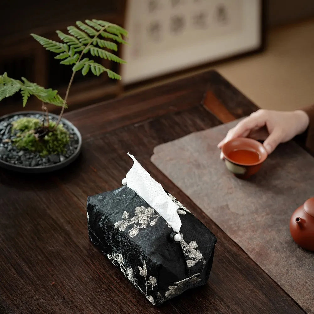 White Chinese brocade tissue box cover with embroidered plum blossoms, shown with and without a pearl buckle.
