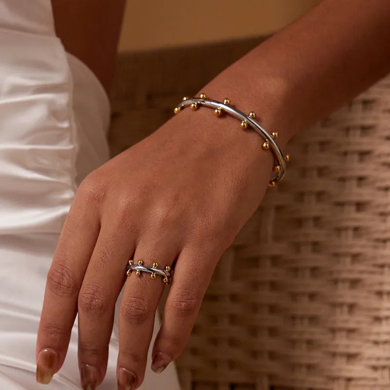 Stainless steel C-shaped charm with textured rivet bean beads on a round alloy bracelet.