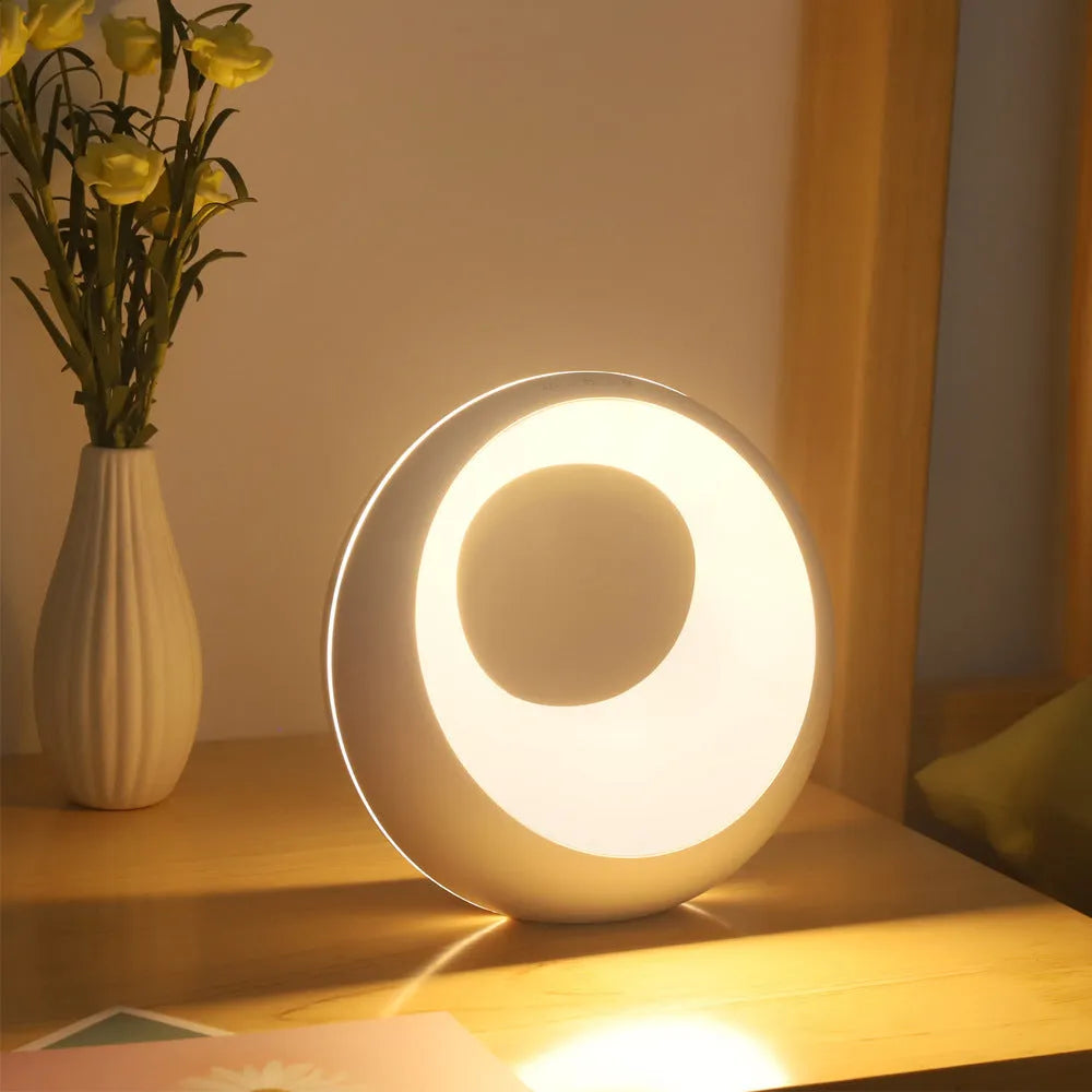 Small white RGB colour changing desk lamp with remote control on a wooden surface.