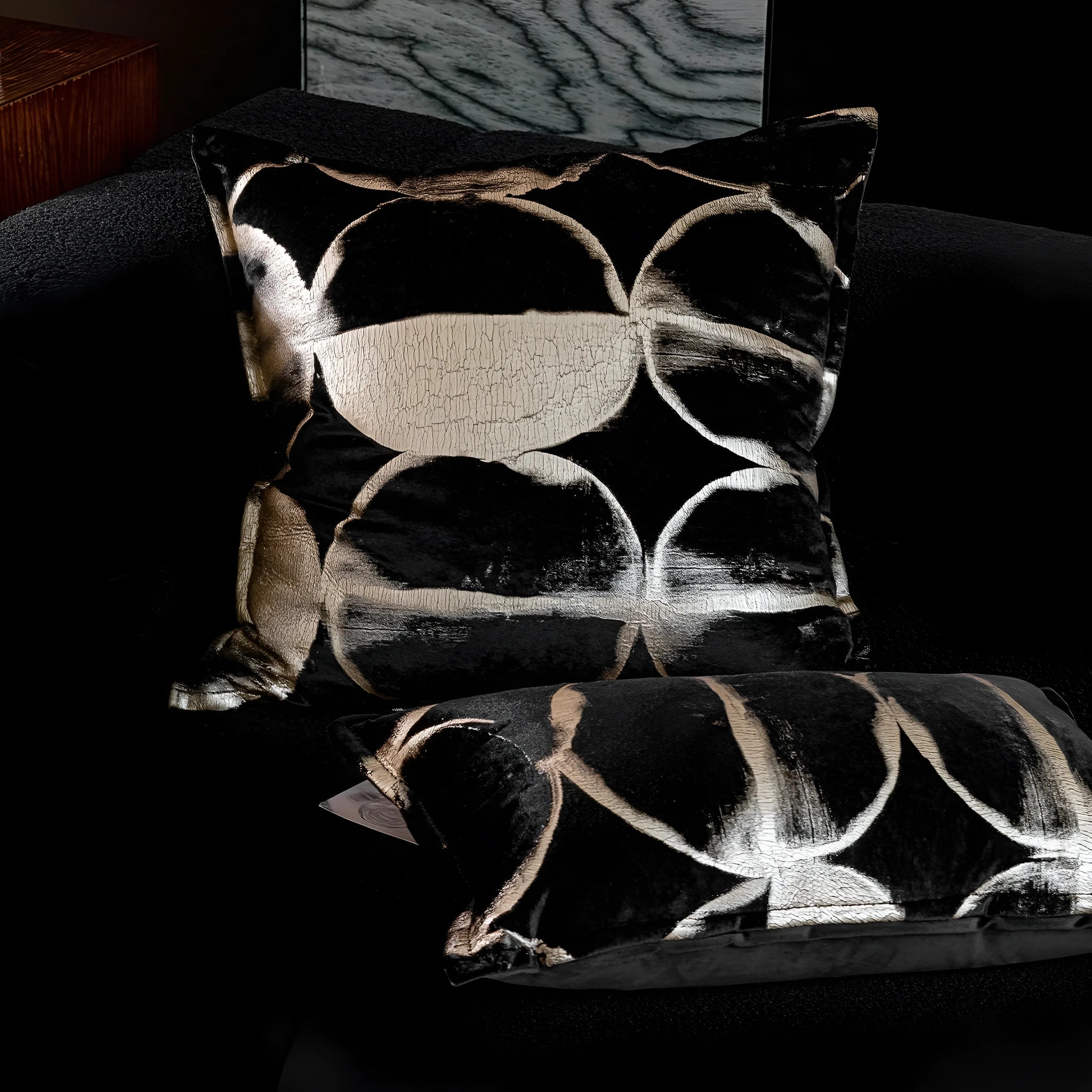 Black and gold abstract patterned square decorative pillow with a flannel cover on a grey sofa.