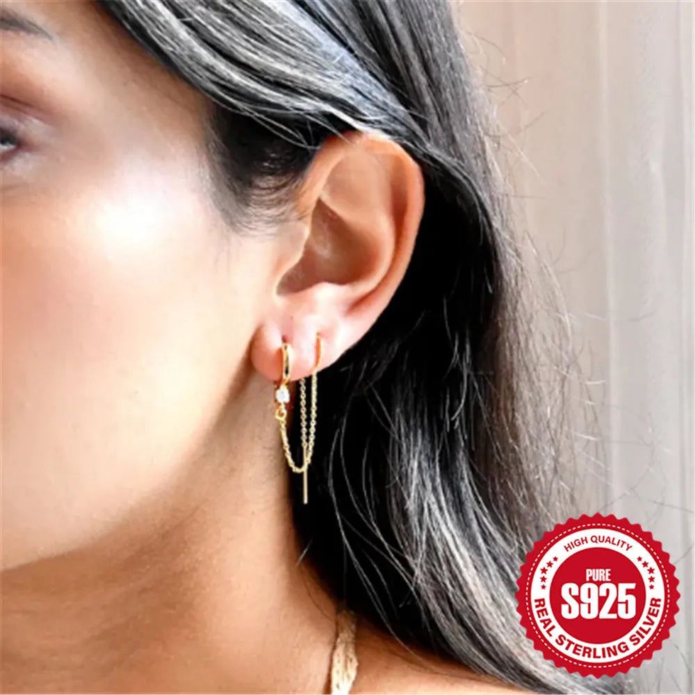Close-up of a sterling silver stud earring with a geometric flower shape and dangling gold-tone tassel and chain details.