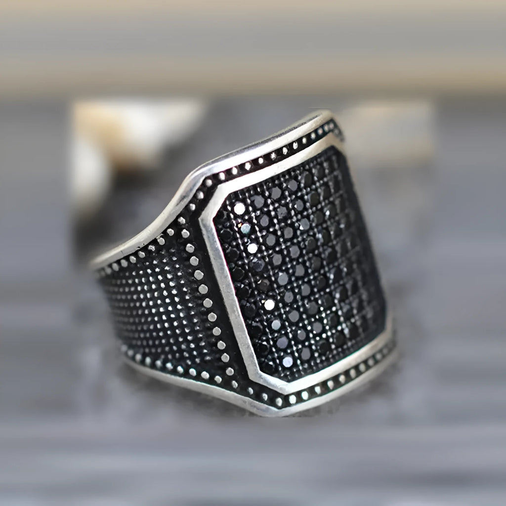 Black alloy ring with copper inlay and zircon stone details, shown on a finger.