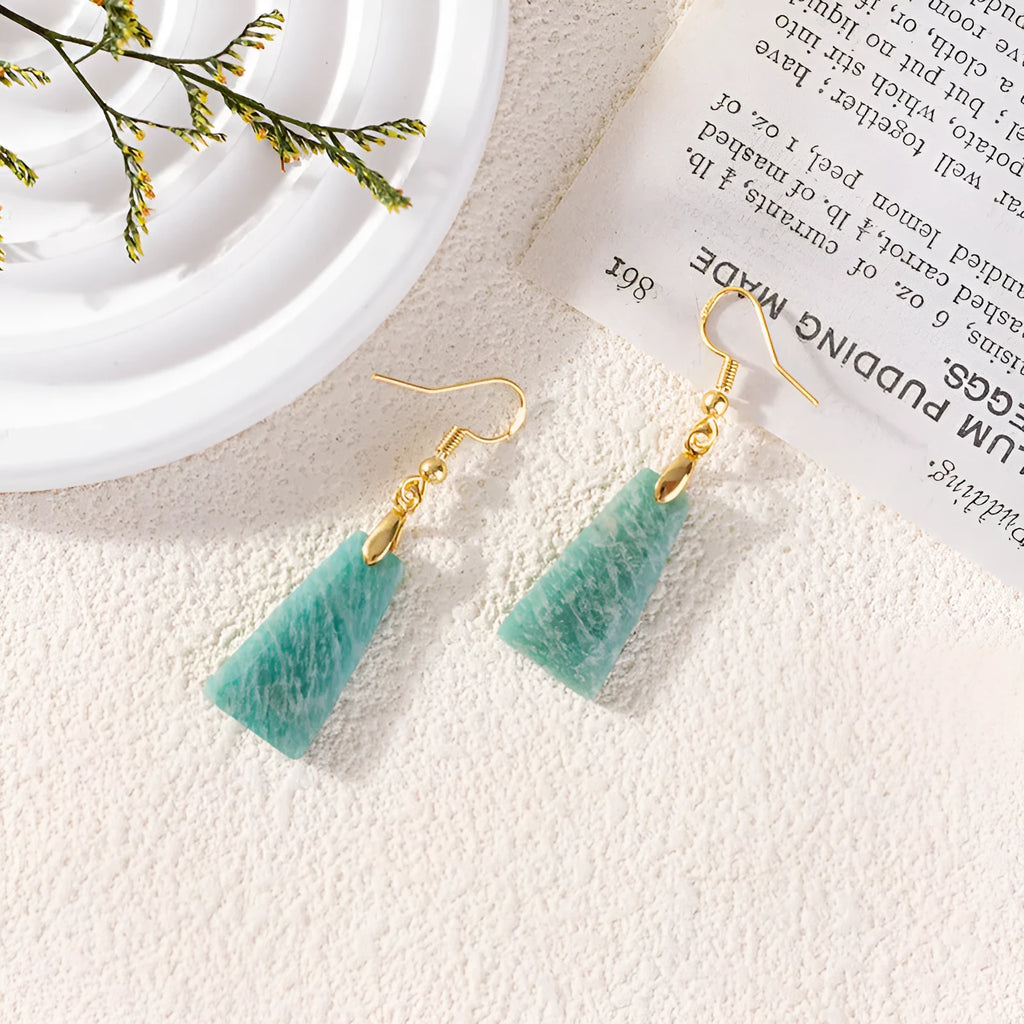 Gold trapezoid earrings with rough-cut amazonite stone and geometric detail on white background.