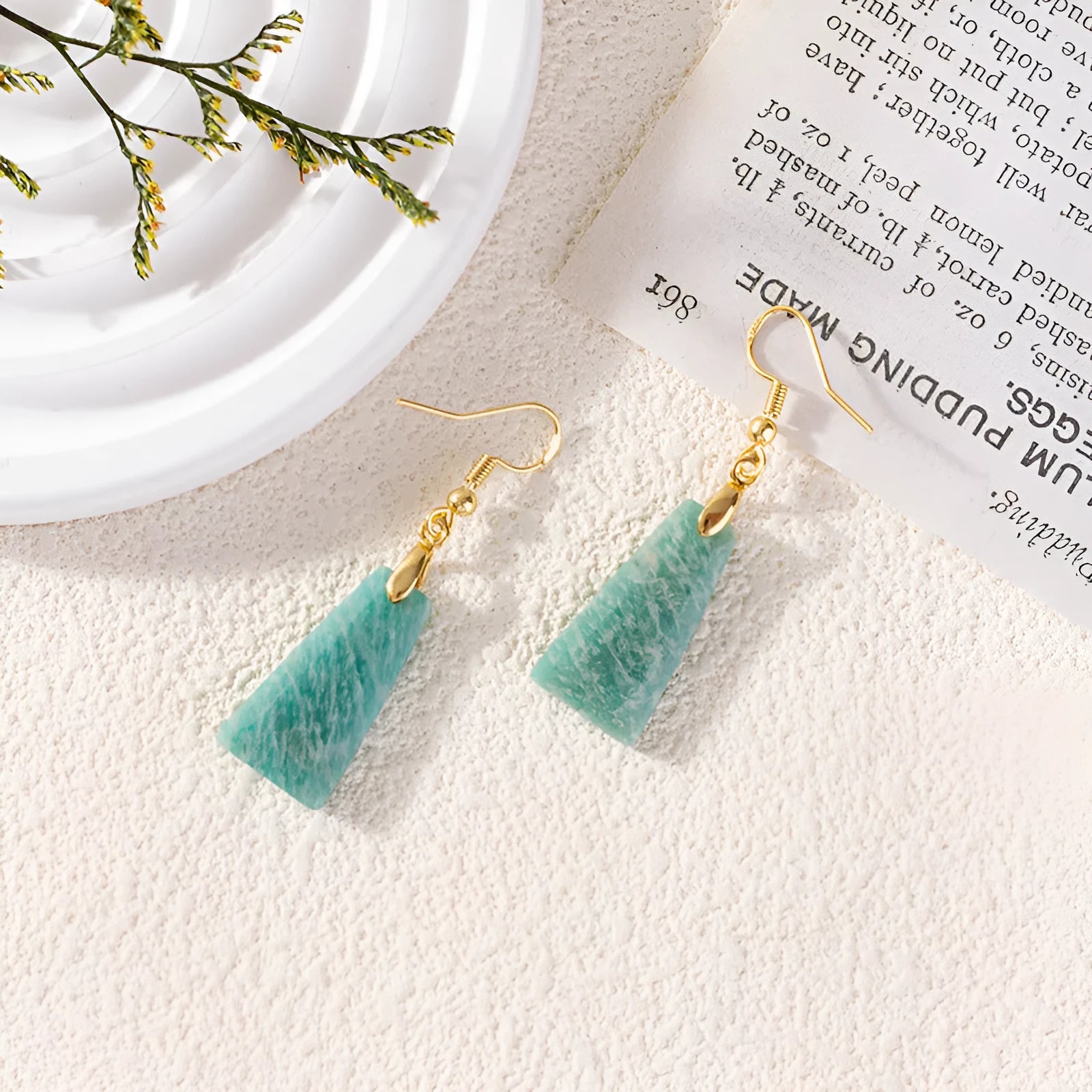 Gold trapezoid earrings with rough-cut amazonite stone and geometric detail on white background.