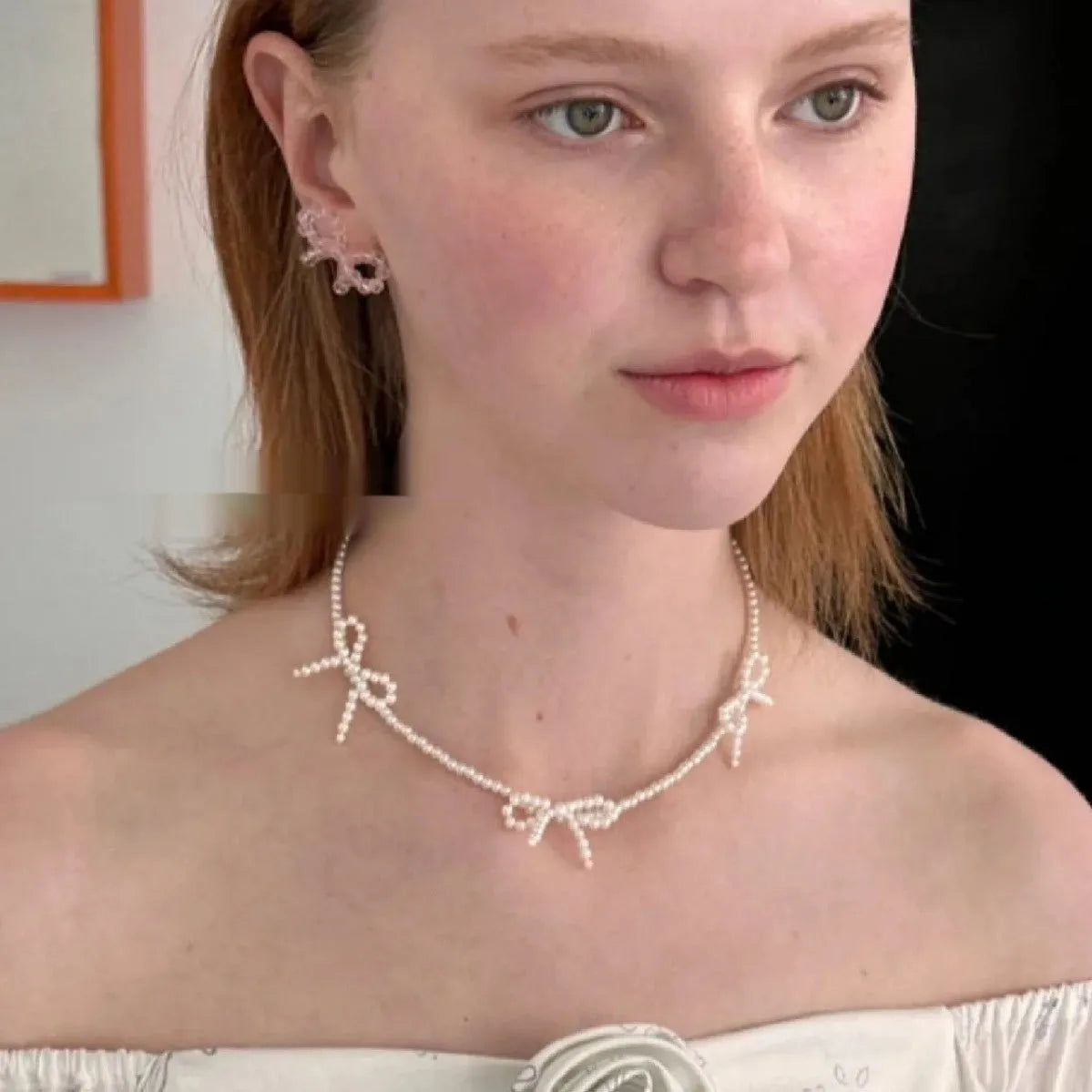 White bow-shaped imitation pearl necklace with an adjustable chain on a woman's clavicle.