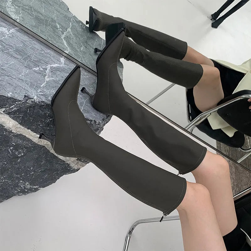 Women's black pointed toe below knee boots with back zipper and stiletto heel on grey background