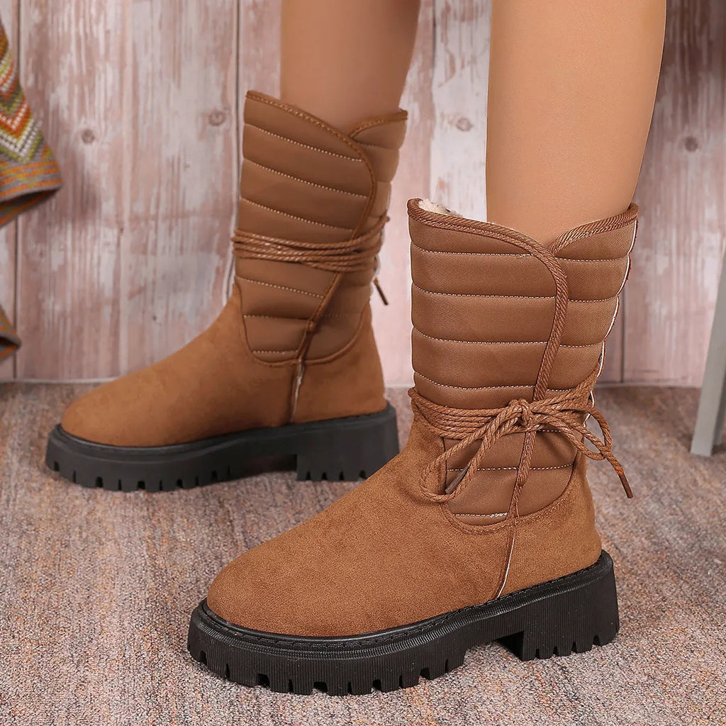 Women's black suede chunky heel snow boots with lace-up front and fleece lining shown on a winter background.