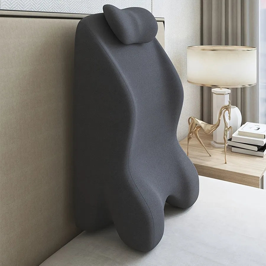 A flat stomach sleeper pillow shown on a bed, designed for prone sleeping and reading.