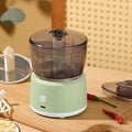 White or light green USB rechargeable mini electric meat grinder with transparent cup on anti-slip pad.