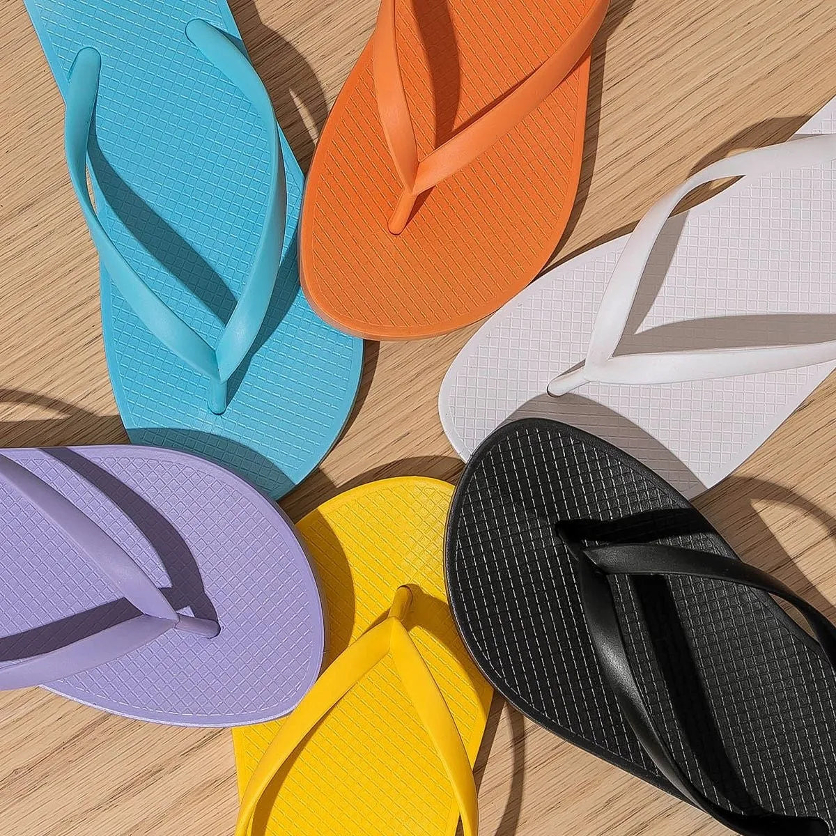 Orange foldable beach slippers with hollow-out design and non-slip PVC soles on a sandy background.