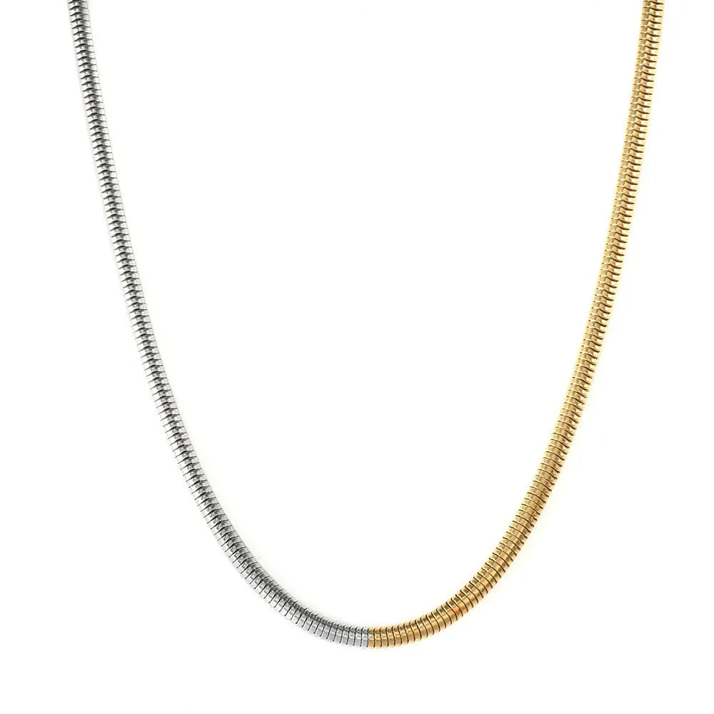 Close-up of a 3mm wide golden snake bone chain necklace with a geometric design on a dark background.