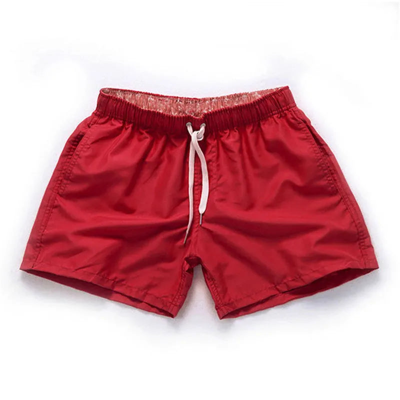 Men's straight-leg beach shorts in emerald green colour on a beach background.