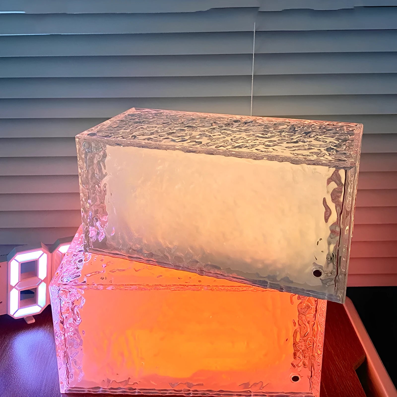 Geometric clear acrylic ice cube shaped night lamp with coloured LED light inside on a wooden table.