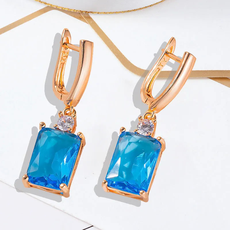 A pair of square-shaped gold-coloured earrings with a geometric design on a white background.