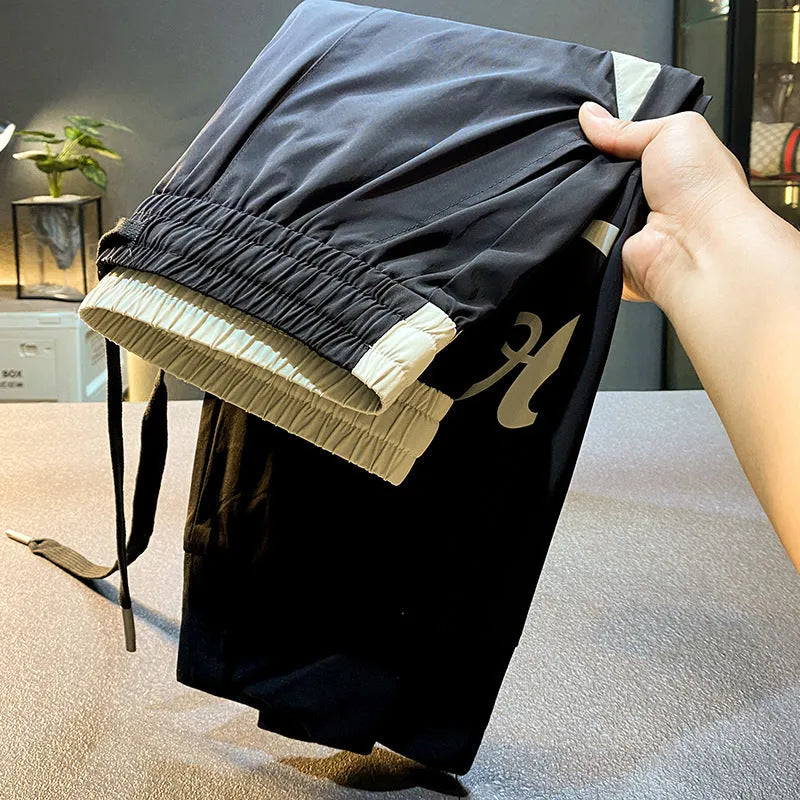 Black cotton men's cropped casual trousers with a banded ankle cuff laid flat.