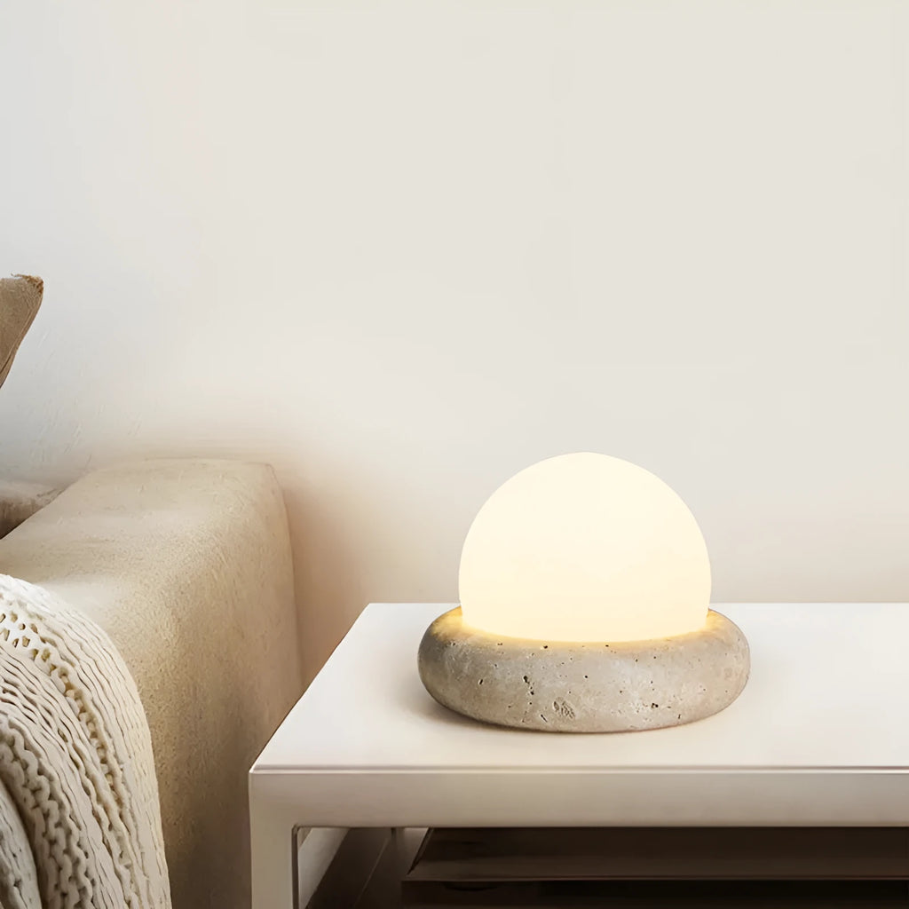 Cream-coloured modern bedside lamp with remote control on a table.