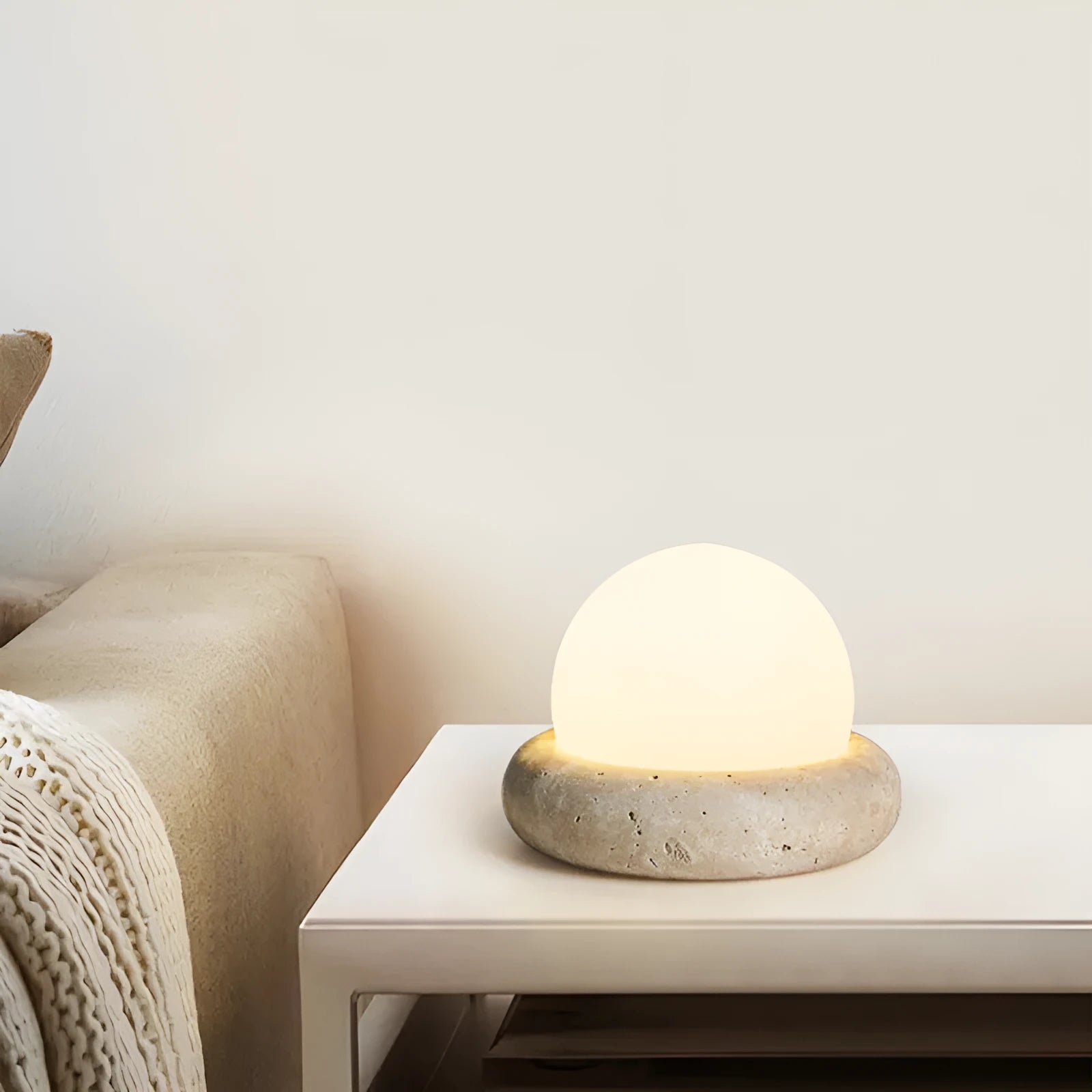Cream-coloured modern bedside lamp with remote control on a table.