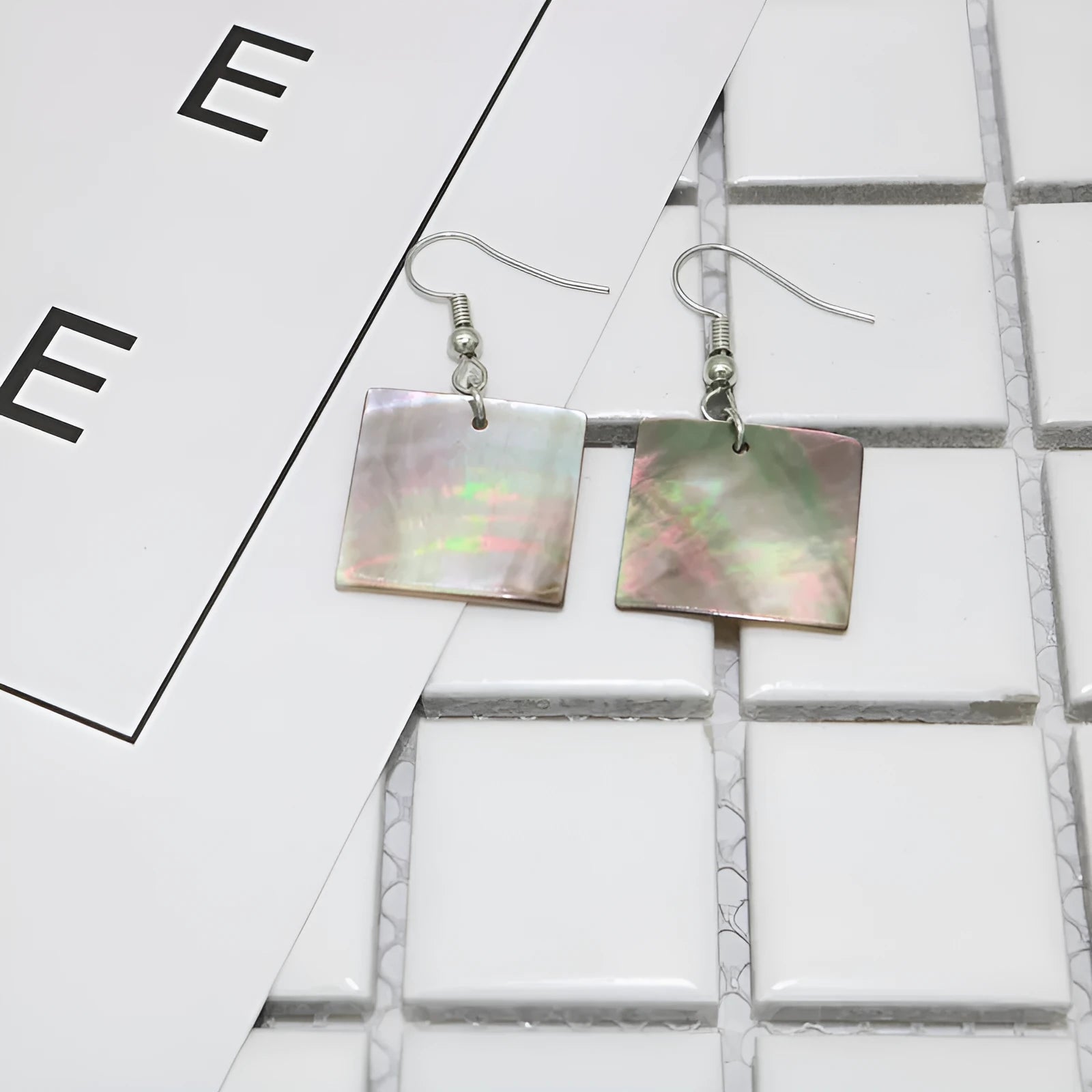 Handmade women's shell earrings in rectangular and square geometric shapes on a neutral background.