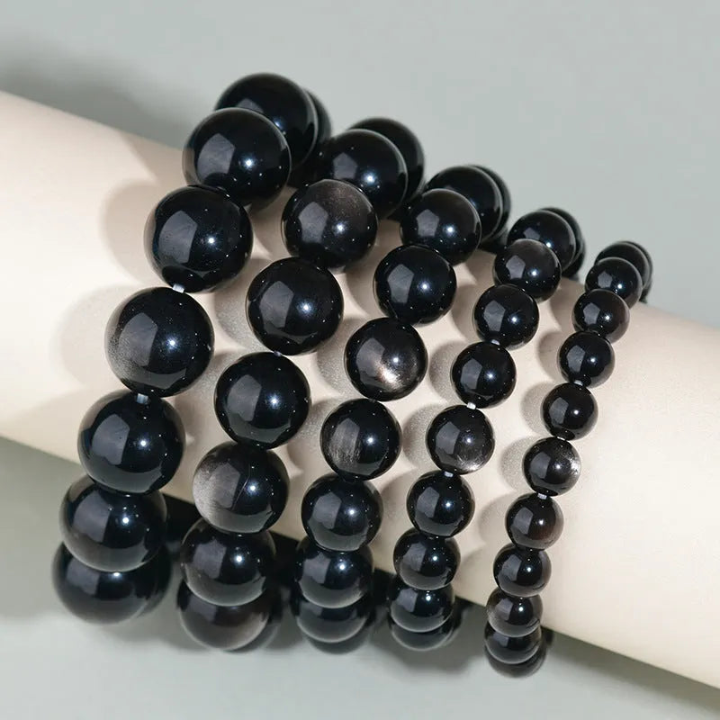 Adjustable sliding knot obsidian bracelet in hand with choice of black, rainbow eye, and silver crystal beads