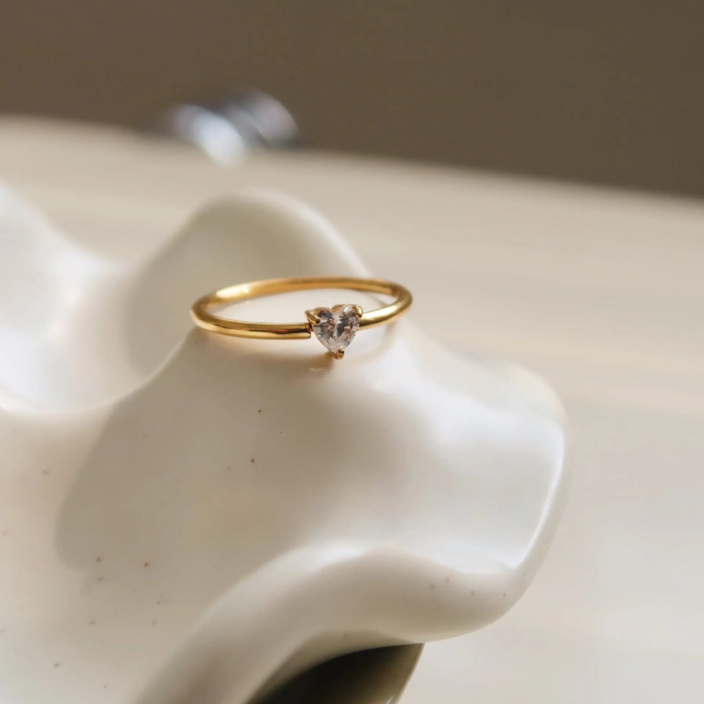 A golden stainless steel ring showing both the love heart design and the oval design option on a hand.