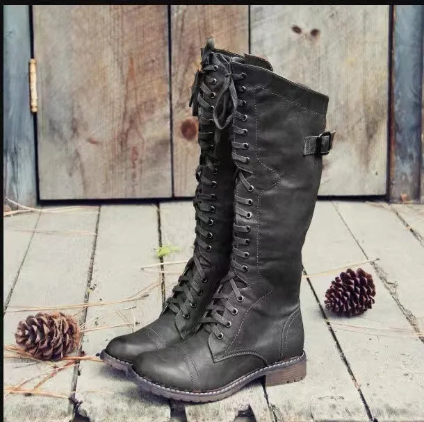 Black chunky heel high leg boot with round toe and low rubber sole on a plain background.