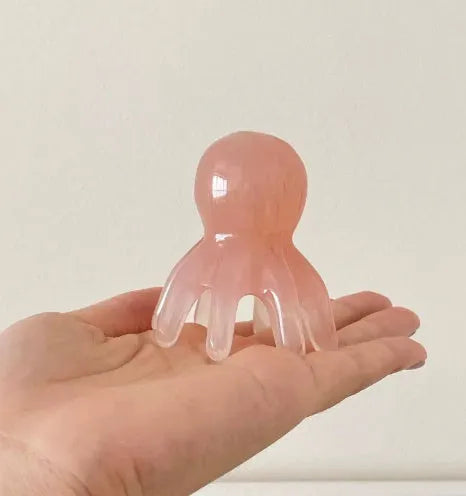 Small pink octopus-shaped natural resin massage comb with storage bag for facial meridian pressure.
