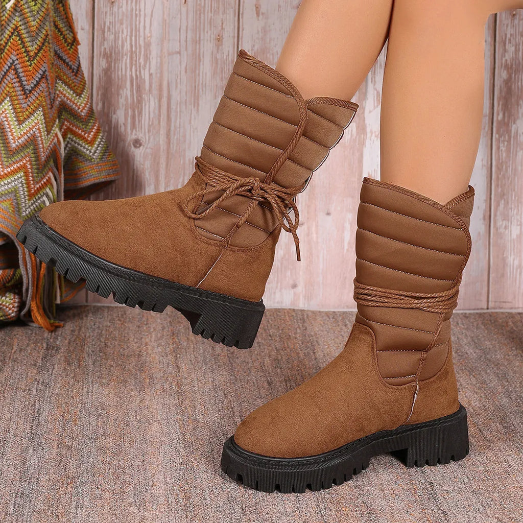 Women's black suede chunky heel snow boots with lace-up front and fleece lining shown on a winter background.