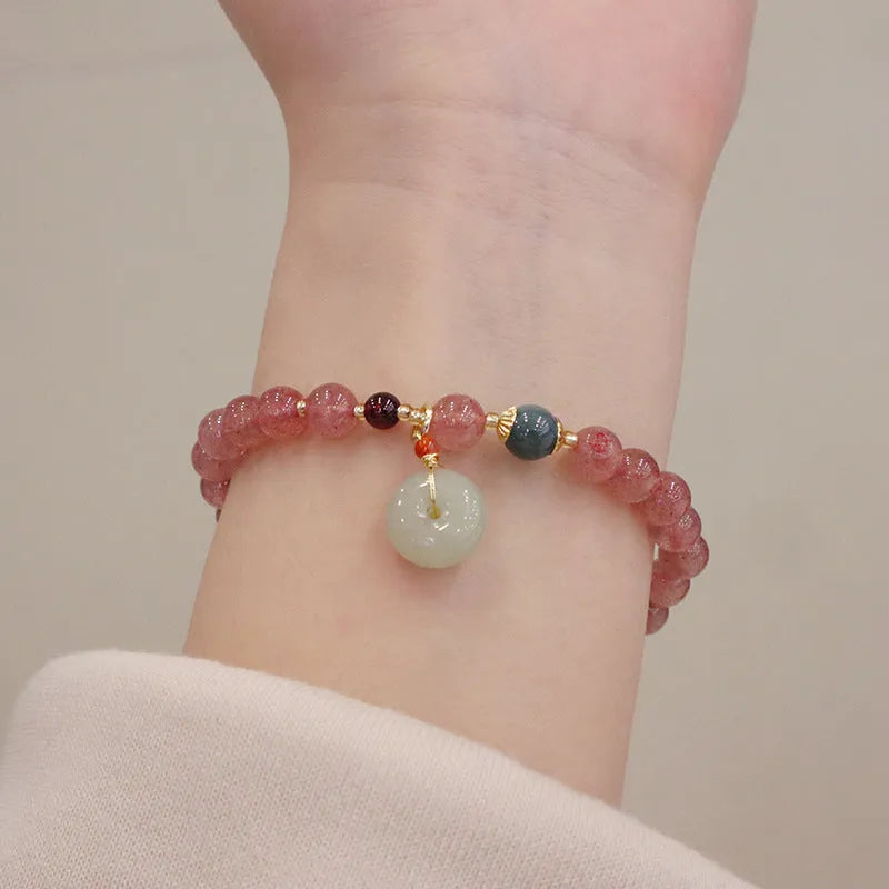 Close-up of a women's strawberry quartz bead bracelet with a geometric pattern and a central gold-tone purse charm.