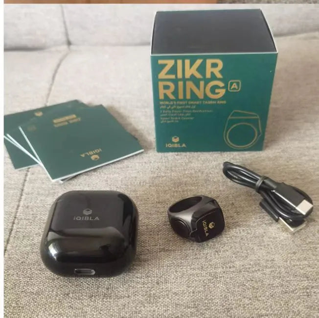 Zikr1 metal smart ring in black with OLED display and single button, shown with charging case.