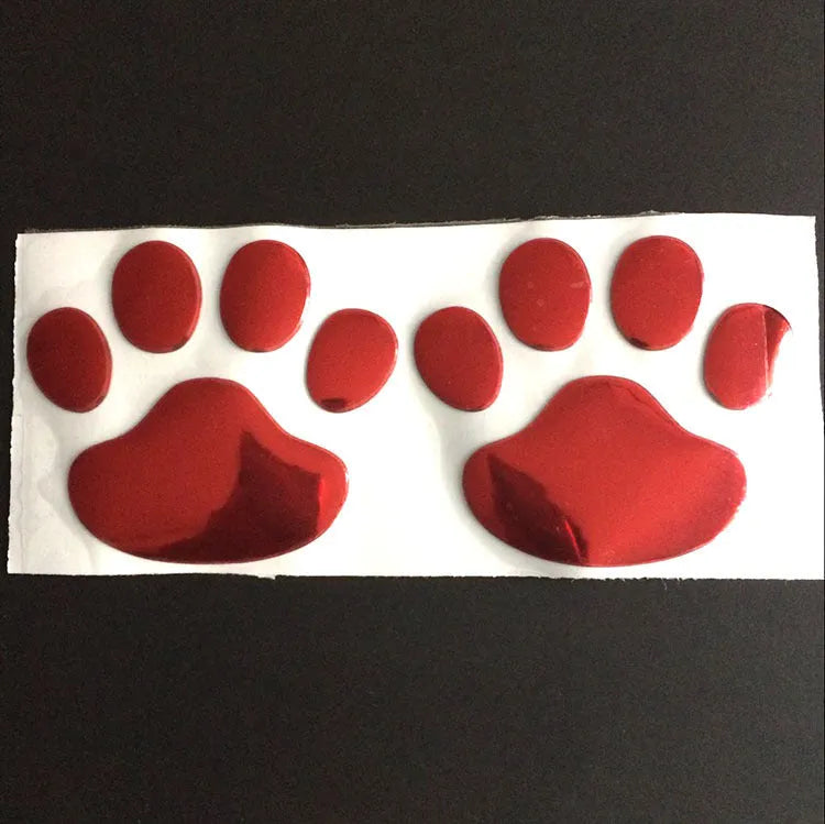 Close-up of a black PVC car sticker with dog footprints and a hand-shaped brush texture on a car bumper.