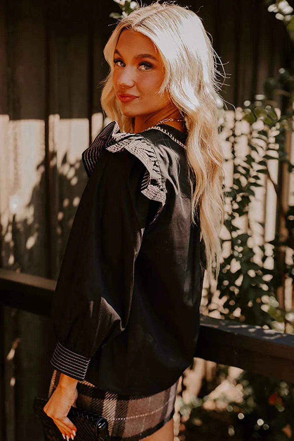 Black women's v-neck blouse with long ruffle sleeves and contrast stitching.