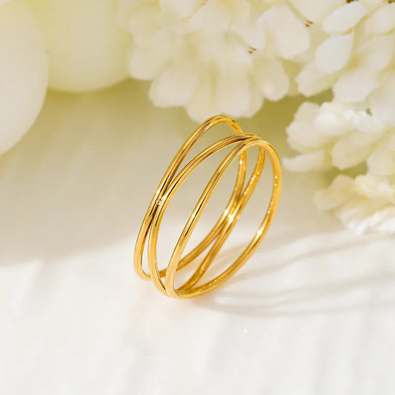 Geometric three-layer coil gold ring on a finger, showing titanium steel construction.
