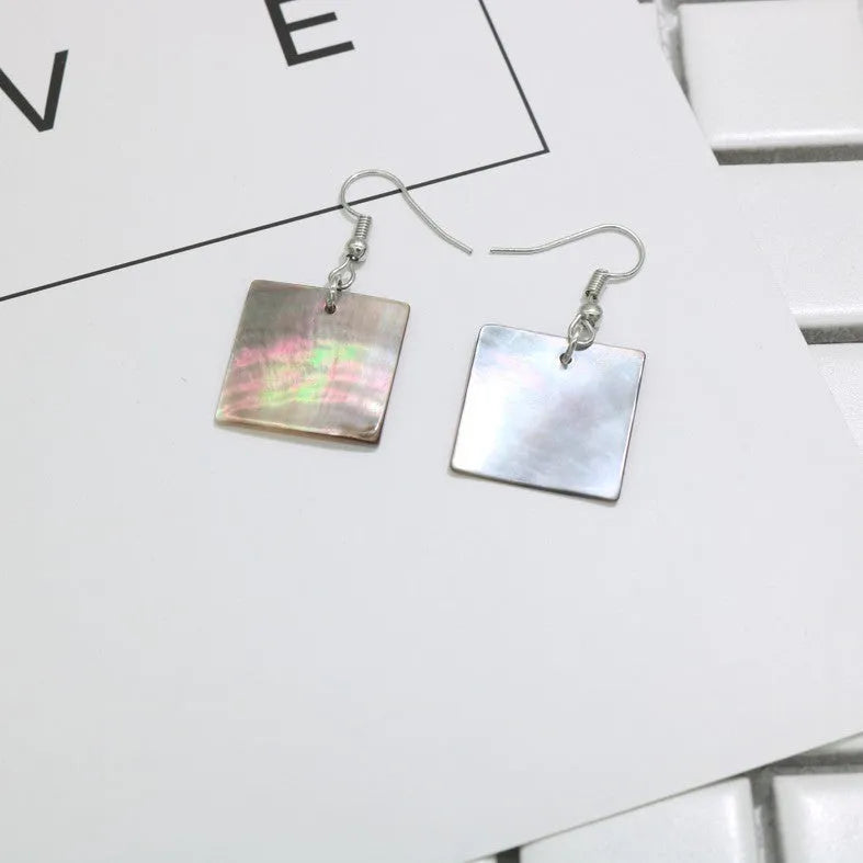 Handmade women's shell earrings in rectangular and square geometric shapes on a neutral background.