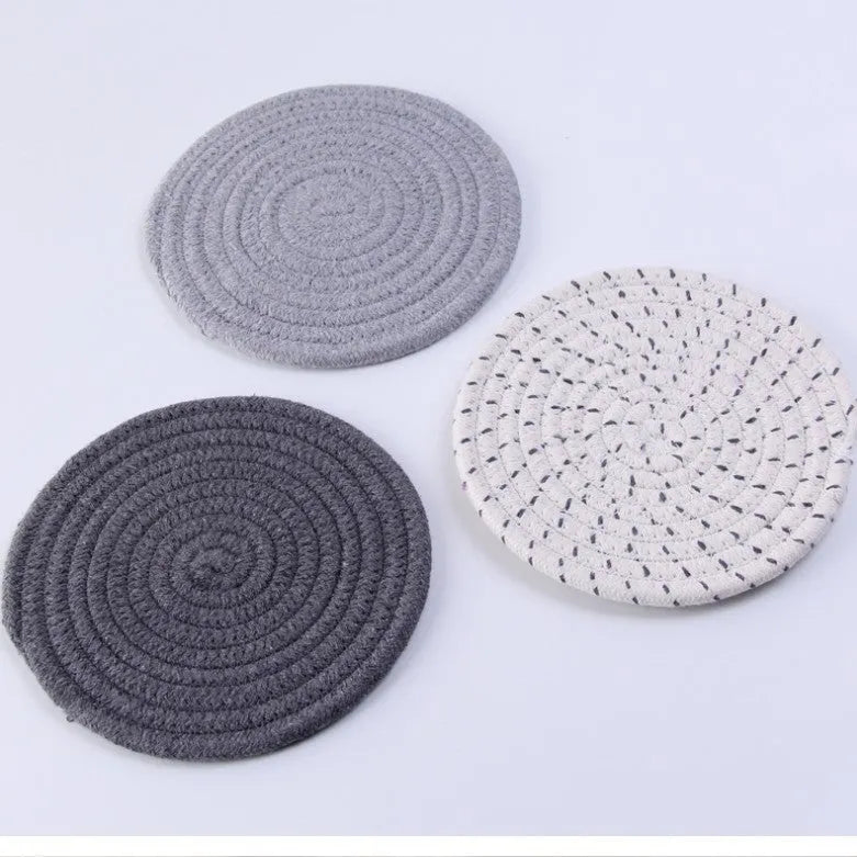 Three round grey cotton cord coasters arranged on a wooden table.